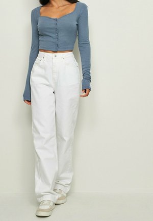 Haut court à rayures bleues avec des détails de boutons et des manches longues, associé à un jean blanc taille haute à jambes larges et des baskets de couleur claire.