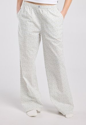 Person wearing loose white pajama pants with small blue and yellow floral prints, hands in pockets, and white socks.