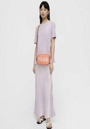 Camiseta de color púrpura claro, falda hasta los tobillos, chanclas negras y un bolso cruzado melocotón con "TOUS" impreso en blanco. Diseño minimalista.