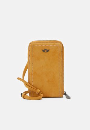 Kleine rechthoekige mosterdgele suède crossbodytas met zichtbare stiksels, metalen logo, ritssluiting en verstelbare band op witte achtergrond.