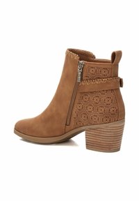 Stivale alla caviglia marrone con una texture liscia, perforazioni decorative sui lati, chiusura con zip e tacco a blocco.