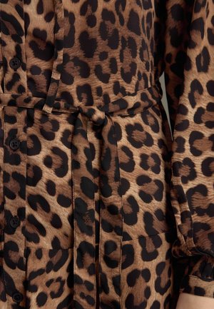 Blusa a stampa leopardata caratterizzata da tonalità marroni e nere, maniche lunghe, dettagli con bottoni e una vita legata per una silhouette definita.