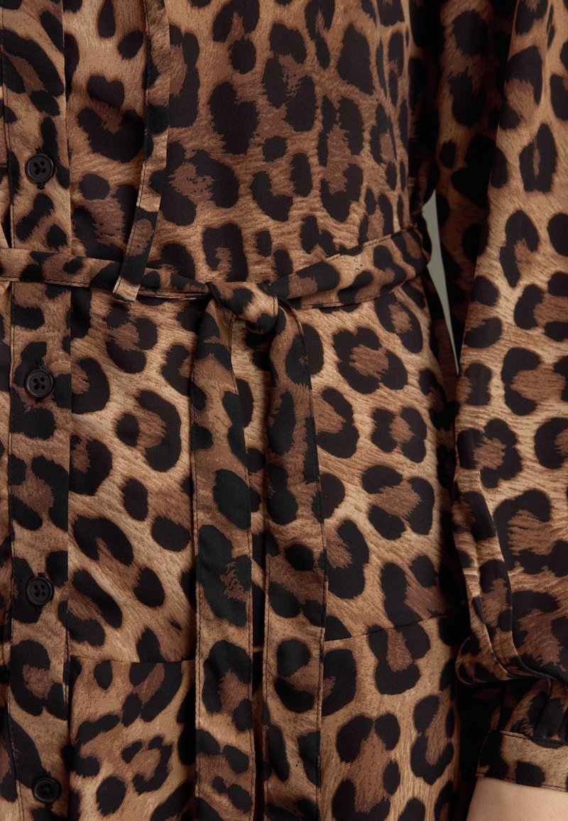 Leopardmönstrad blus med bruna och svarta nyanser, långa ärmar, knapplister och knytband i midjan för en definierad silhuett.