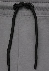 Cordon noir noué sur une ceinture élastique grise d’un pantalon en tissu avec des détails de couture visibles.