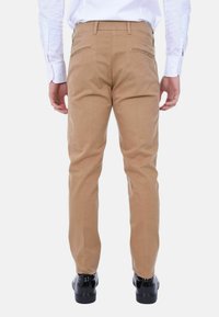 Chino beige con design a gamba dritta, caratterizzati da una texture morbida, passanti per cintura e due tasche posteriori. Abbinati a scarpe nere.