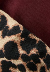 Leopardenmustertextil in Beige mit schwarzen flecken, neben einem glatten burgunderfarbenen Stoff, der eine kontrastierende visuelle und taktile Oberfläche schafft.