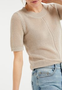 Beige, stickad tröja med korta ärmar, rund halsringning och texturerade ränder. Har en avslappnad passform och subtila sömdetaljer.