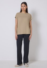 Top corto de algodón en color marrón claro con un diseño cosido en el pecho, combinado con pantalones de pierna ancha texturizados en color marino y zapatos casuales.