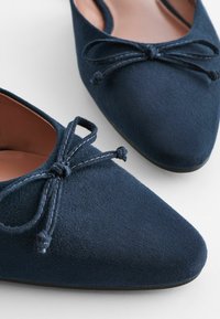 Ballerines en daim bleu marine avec des bouts pointus et des accents de nœud décoratifs. Dotées d'une doublure intérieure lisse et d'une semelle flexible pour un confort optimal.