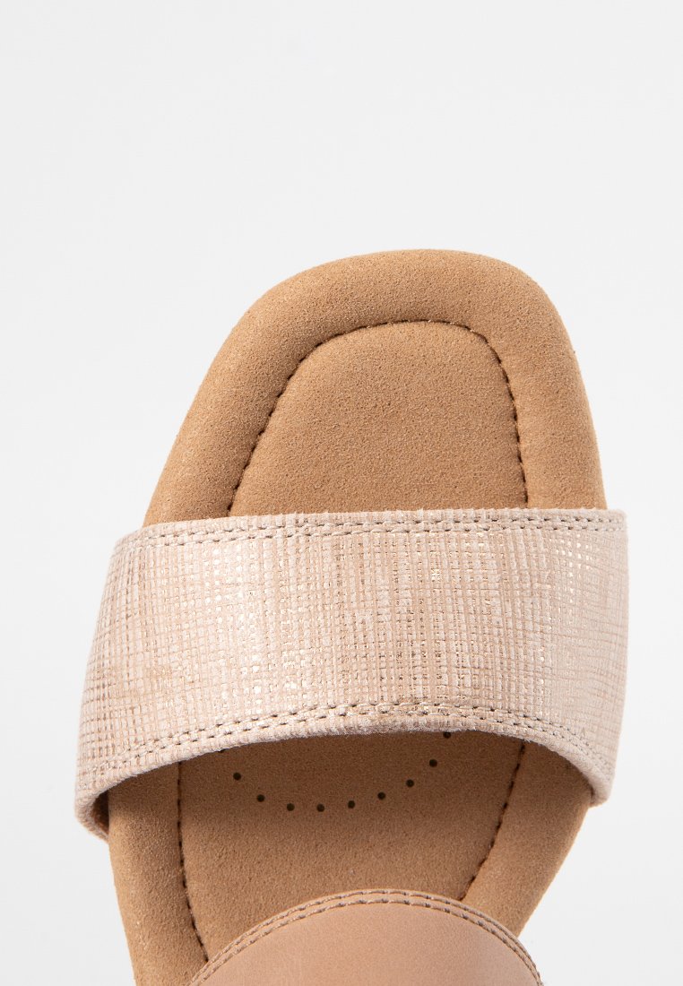 Sandal de color beige con una correa metálica texturizada, plantilla de ante suave, punta redonda y costuras detalladas a lo largo de los bordes.