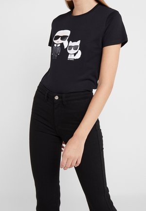 Camiseta de algodón negra con un gráfico de dos figuras de dibujos animados con gafas de sol, una vestida con un traje y la otra con una silueta de gato.