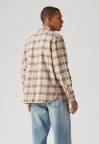 Camisa de manga longa xadrez em tons de bege e azul, apresentando um colarinho dobrável, punhos abotoados e uma bainha curved.