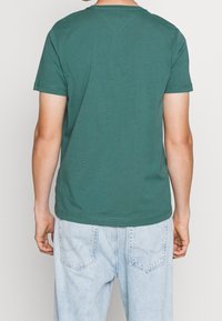 Camiseta de algodón verde con un cuello redondo clásico y mangas cortas, que presenta un dobladillo recto y detalles de costura mínimos en la parte posterior.