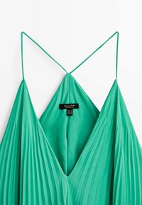 Robe verte plissée sans manches avec de fines bretelles spaghetti et un décolleté en V, montrant une étiquette de vêtement à l'intérieur du dos.