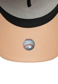Breskva kapa za bejzbol s crnim vizirima, s kružnom MLB naljepnicom u središtu. Tekstura je glatka s vidljivim detaljima šivanja.