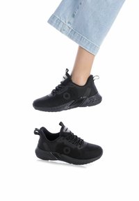Zapatillas deportivas negras con parte superior de malla, acentos texturizados y suela acolchada. Cordones y un lazo en el talón para facilitar el uso.
