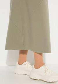 Khaki midi sukně s geometrickými švy v kombinaci s bílými chunky teniskami. Hladká textura, ležérní design a délka po kotníky.