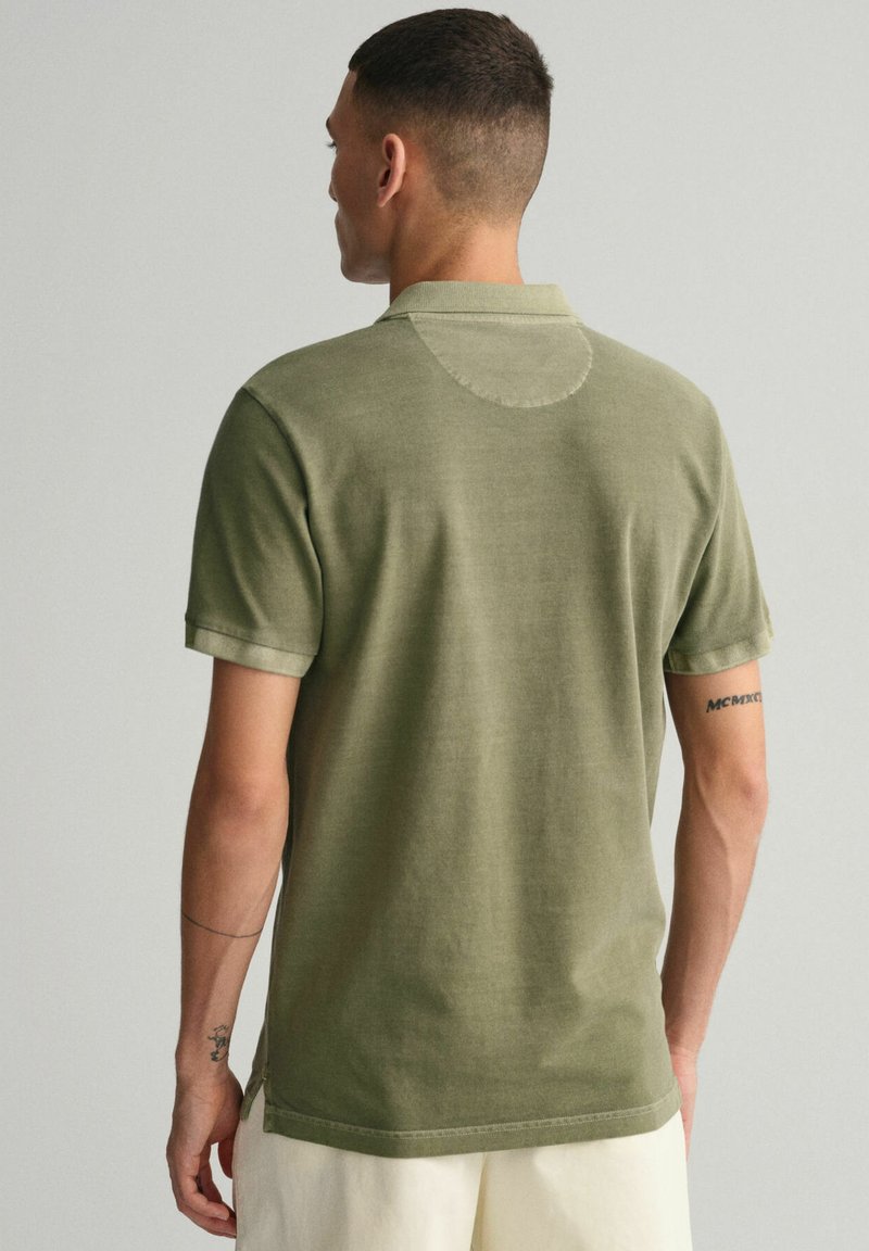 Polo en coton vert olive avec des manches courtes, un col en côtes et un détail circulaire brodé à l'arrière.
