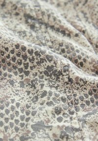 Gros plan sur un tissu à motif peau de serpent dans des tons beige, gris et noir, montrant une texture détaillée et des coutures visibles.