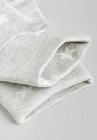 Grauer Baumwollstoff mit weicher Textur, der ein Sternmuster in Weiß zeigt. Der Stoff ist gefaltet und zeigt die Kante sowie die Designdetails.