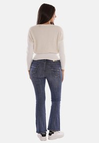 Maglione a maglia crema con retro testurizzato, abbinato a jeans a zampa d'elefante in denim scuro con tasche posteriori. Sneakers con accenti neri e suola bianca.
