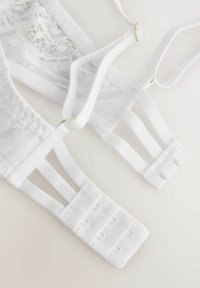 Spate sutien alb din dantelă și plasă, cu bretele reglabile și închidere cu croi cu trei rânduri de cârlige pe un fundal deschis.