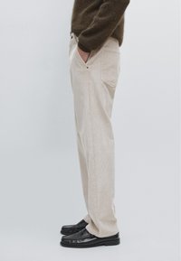 Pantalons en velours côtelé beige avec des poches latérales, une coupe décontractée et une texture lisse, associés à des mocassins noirs.