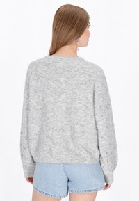 Szürke kötött pulóver laza szabással, színes foltokkal és bordás mandzsettákkal. Világoskék farmer rövidnadrággal viselve.