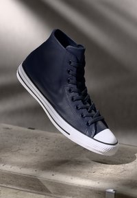 Pantofi sport înalți din piele bleumarin, cu vârf din cauciuc alb, șireturi texturate și dungi contrastante alb-negru pe talpă.
