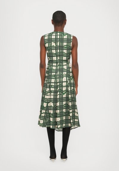 Rochie verde cu carouri, cu un design fără mâneci, talie strânsă și fustă evazată. Prezintă accente crem și este purtată cu colanți negri și tocuri.