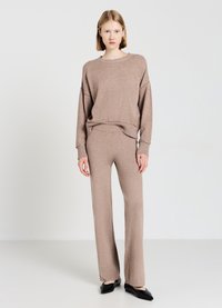 Maglione beige a maglia con spalle scese, abbinato a pantaloni larghi coordinati. Il tessuto è morbido e la silhouette è rilassata. Le ballerine nere completano il look.