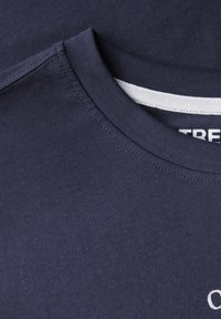 Granatowa bawełniana koszulka z okrągłym dekoltem, z białą metką wewnętrzną i gładką fakturą. Zawiera mały haftowany detal.