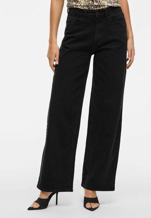 Schwarze weite Jeans mit hoher Taille, aus Denim gefertigt. Verfügt über Fronttaschen und eine lockere Passform. Kombiniert mit schwarzen offenen Absatzschuhen.