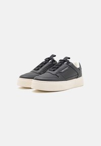 Sorte lærersneakers med teksturert overflate, featuring en hvit klumpete såle og svarte snøring, samt en side logo detalj.