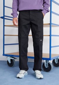 Svarta byxor med rak passform, med fickdetaljer och en märkespatch. Tyget verkar hållbart, tillsammans med lätta sneakers.