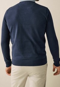Maglione a collo tondo di colore blu navy, realizzato in maglia con maniche lunghe, polsini e vita a costine, presenta una texture liscia e un design aderente.