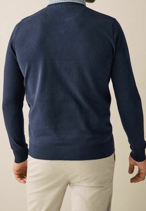 Pull en maille bleu marine avec manches longues, poignets et taille côtelés, présentant une texture lisse et une coupe ajustée.
