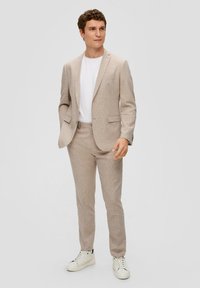 Beige geruite pak met een getailleerde pasvorm, gemaakt van een textuur stof. Gecombineerd met een wit t-shirt en witte sneakers voor een casual look.