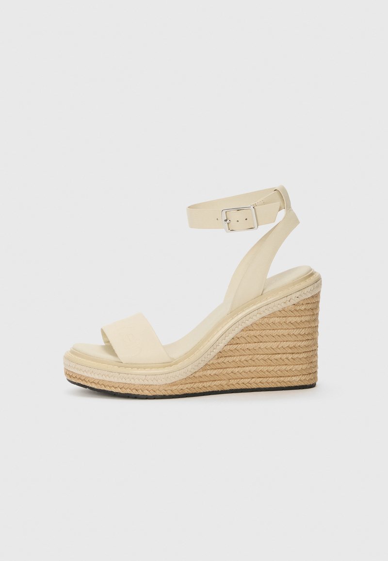 Beige veskesandaler med en glatt læroverdel, bred tårem, ankelrem med spenne og en strålignende teksturert kilehæl.