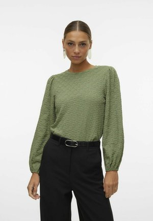 Groene getextureerde blouse met lange mouwen en pof-schouders, gecombineerd met zwarte high-waisted broeken en een zwarte riem met een zilveren gesp.