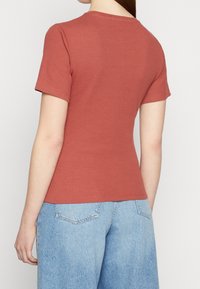 Košile s krátkým rukávem v rezavé barvě s ribbed texturou a kulatým výstřihem, zkombinovaná se světle modrými džínami s vysokým pasem. Jednoduchý, přiléhavý design.
