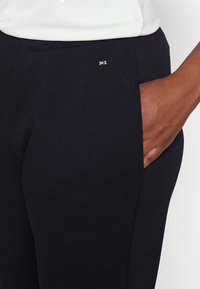 Marineblauwe sportbroek met een zijzak, gemaakt van zachte stof. Heeft een klein logo-accent nabij de tailleband. Soepele textuur.