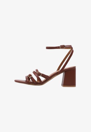 Sandalia marrón de punta abierta con tres tiras delanteras con hebillas doradas, una correa en el tobillo y un tacón ancho.
