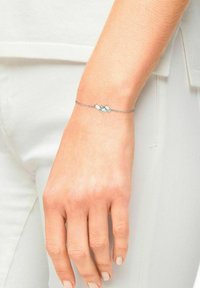 Silver bracelet featuring geometric design with three clear gemstones set in a central focal point, accentuating a delicate chain.