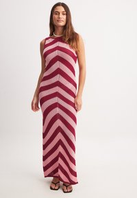 Maksikleit zigzag-mustriga, millel on vahelduvad punase ja roosa toonid. Õlakuju disain, tekstureeritud kudumiga kangas ja liibuv siluett.