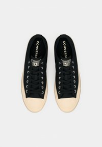 Black canvas sneakers with a cream rubber toe cap. Features white metal eyelets, black laces, and a branded tongue label.