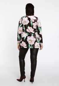 Langærmet bluse med blomstermønster, hvor lyserøde og grønne blomster pryder en mørk baggrund. Kombineret med sorte læderbukser og brune hæle.