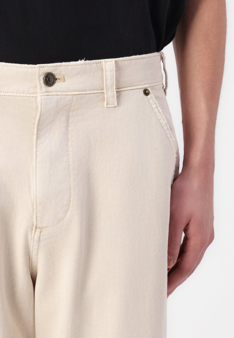 Beige Jeans mit geradem Schnitt, ausgestattet mit einem Knopfverschluss, tonalem Nähen und Seitentaschen. Glatte Textur mit feiner Maserung.