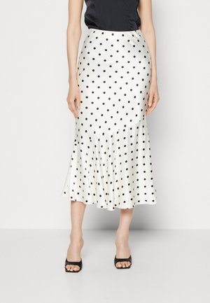Woman wearing a white midi skirt with black polka dots and flared hem, paired with black open-toe high-heeled shoes and a black top.