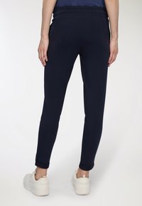 Granatowe dresowe spodnie o luźnym kroju, z elastycznym pasem i podwiniętymi mankietami, wykonane z gładkiego, lekkiego materiału, zestawione z białymi trampkami.